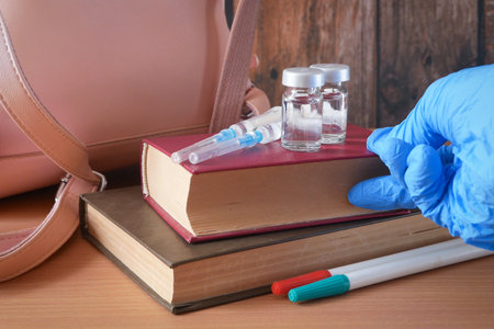 doctor puts in table bottles and syringes of vaccine aganist covid-19 near book pile and school supplies, back to school in coronavrus time conceptの写真素材