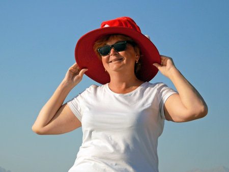 Funny senior woman wearing santa claus hat over sun hat on the sea beach, woman dancing and wishes a merry Christmas and happy new year Outdoorsの写真素材