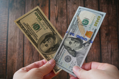Hand holds new and old 100 dollar banknotes on wooden background, conceptの写真素材