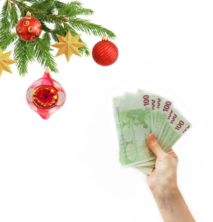 Cristmas greeting card with new year balls and decorations and hand holding big stack of euro money, merry christmas and happy new year, wealth in new year conceptの写真素材