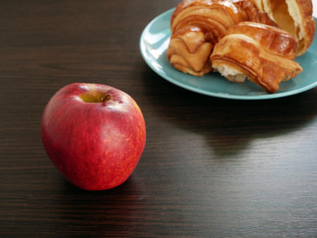 Red apple and croissants in plate on wooden background. Apple vs croissants, healthy food vs unhealthy food, Closeupの写真素材