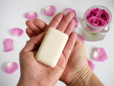 organic soap bar in hand on roses and petal and white background, oil rose for natural cosmetic, top...