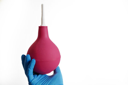 Doctor in blue medical gloves holding red enema isolated on white background, concept, closeupの写真素材