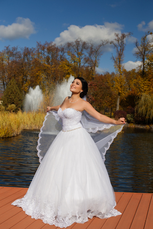A happy bride in a rich wedding dress is standing on the pierの写真素材
