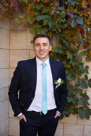 Happy bridegroom in a stylish suit against a brick wall backgroundの写真素材