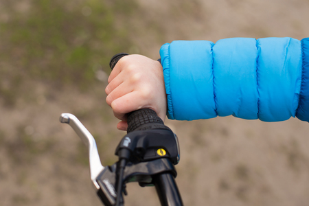A boy in a blue jacket holds a bicycle handlebars.の写真素材