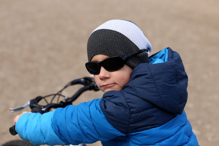 A boy in a blue jacket holds a bicycle handlebars.の写真素材