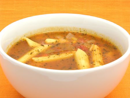Noodle soup with tomatoes and herbs on orangeの写真素材