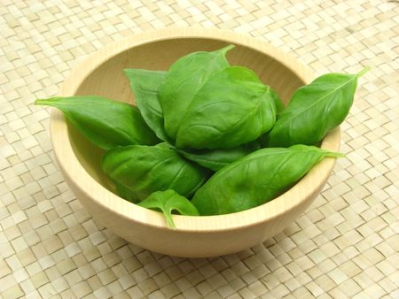 Wooden bowl with basil on rattan underlayの写真素材
