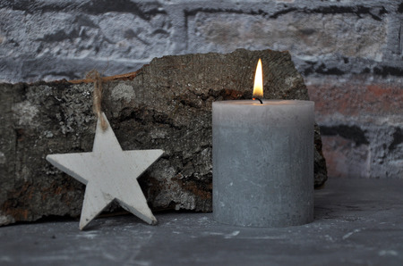 Burning candle, star and wood billet in front of brick wallの写真素材