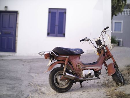 an old rusted red scooter in Greece with blue door and windowの写真素材