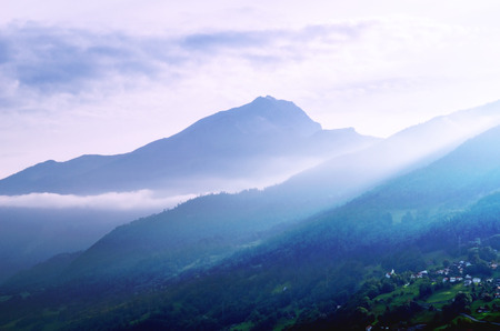 Mountains in Mist, lit by Evening Sun, with a Village below. Stylized Fairy Landscape. Photo taken in Rhine Valley, Switzerland.の写真素材