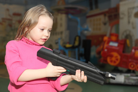 cute little smiling girl playing with the big pistolの写真素材