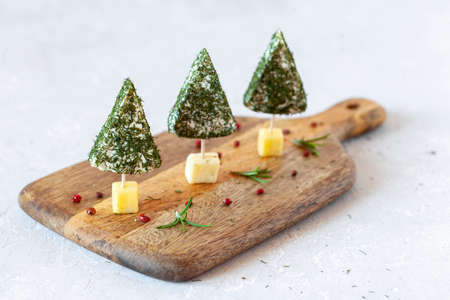 Christmas trees appetizers made of soft cheese on a cutting board on white background, closeup, side viewの写真素材