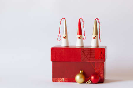 three Santa Clauses figurines on a red gift box, decorative new year tree balls, white background, side view, copy spaceの写真素材