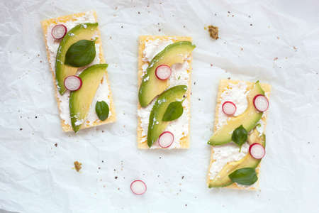 crisp toasts gluten free with soft cheese, avocado, radish and basil on the white background, top...