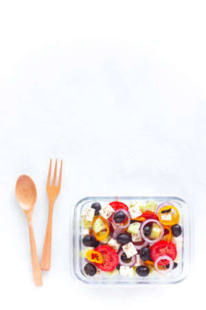 container with greek salad, wooden cutlery, on white background, top view, copy space, concept of healthy food and zero wasteの写真素材