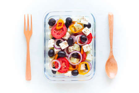 container with greek salad, wooden cutlery, on white background, top view, concept of healthy food and zero wasteの写真素材