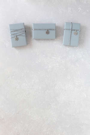 three gray gift boxes decorated with silver ribbon and snowflake pendant, on gray background, top view, copy spaceの写真素材