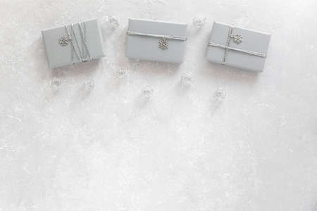 three gray gift boxes decorated with silver ribbon and snowflake pendant, on gray background, top...