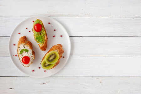 three homemade bright mini sandwichs with cream cheese and vegetables, on a white plate on wooden background, top view, copy spaceの写真素材