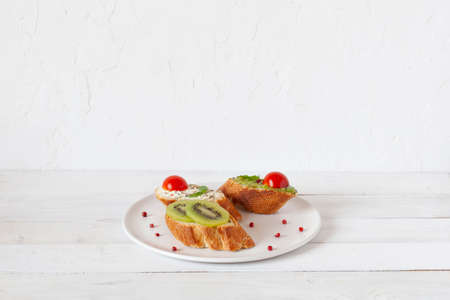three homemade bright mini sandwichs with cream cheese and vegetables, on a white plate on wooden background, side view, copy spaceの写真素材