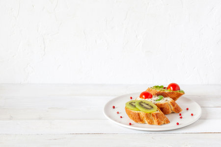 three homemade bright mini sandwichs with cream cheese and vegetables, on a white plate on wooden background, side view, copy spaceの写真素材