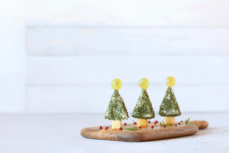 appetizer of new year trees made of cheese and decorated with dill and grapes, easy cooking, on the wooden cutting board, side view, copy spaceの写真素材