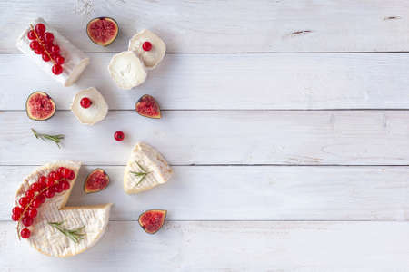 camembert and goat cheese decorated with slices of fig fruits, red currants and rosemary, on white wooden background, top view, copy spaceの写真素材