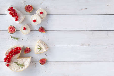 camembert and goat cheese decorated with slices of figue fruits, red currants and rosemary, on white wooden background, top view, copy spaceの写真素材