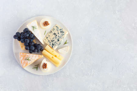 Cheese plate served with grapes and walnuts on a gray concrete background, top viewの写真素材