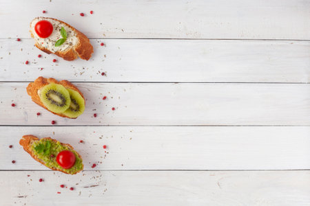 three homemade bright mini sandwichs with cream cheese and vegetables, on white wooden background, top view, copy spaceの写真素材