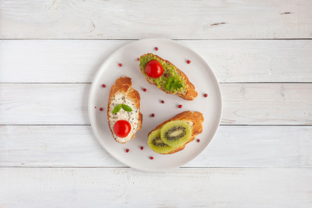 three homemade bright mini sandwichs with cream cheese and vegetables, on a white plate on wooden background, top viewの写真素材
