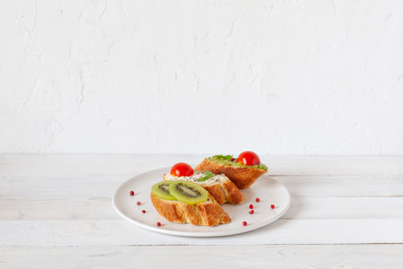 three homemade bright mini sandwichs with cream cheese and vegetables, on a white plate on wooden background, side view, copy spaceの写真素材
