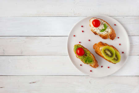 three homemade bright mini sandwichs with cream cheese and vegetables, on a white plate on wooden background, top view, copy spaceの写真素材