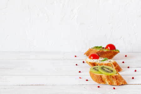 three homemade bright mini sandwichs with cream cheese and vegetables, on wooden background, side view, copy spaceの写真素材