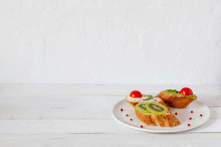 three homemade bright mini sandwichs with cream cheese and vegetables, on a white plate on wooden background, side view, copy spaceの写真素材