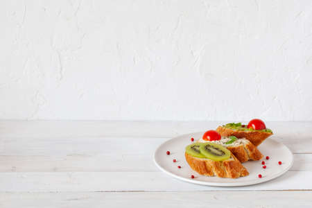 three homemade bright mini sandwichs with cream cheese and vegetables, on a white plate on wooden background, side view, copy spaceの写真素材