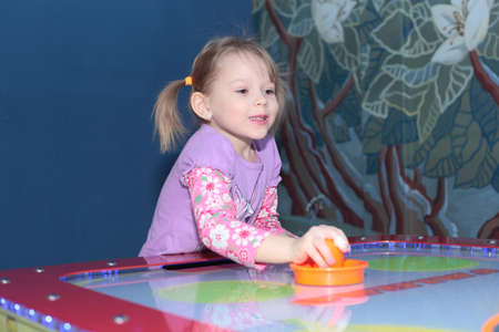 cute little blond girl playing air hockeyの写真素材