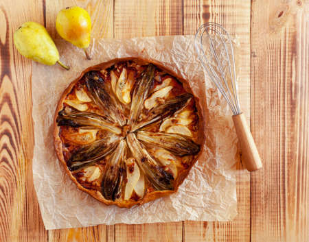 Cooking of chicory, pear and gorgonzola tart, wooden background, top viewの写真素材