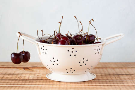 cherries in a white enameled strainer on the wooden backgroundの写真素材