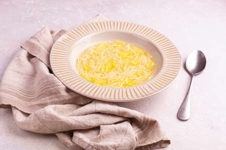 portion of potato and pasta soup in a plate on a table, cotton napkin, spoon, side viewの写真素材