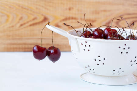 cherries in a white enameled strainer on the wooden backgroundの写真素材