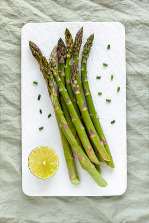 Asparagus stems on the white plate served with green lemon and cut chivesの写真素材
