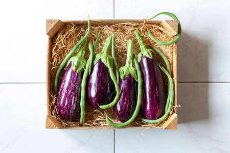 Eggplants and green beans in a vegetable wooden case on tiles backgroundの写真素材