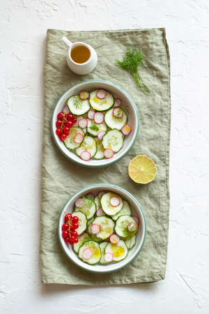 radish and cucumber salad served in a two bowls on the linen napkin and decorated with red currants, top viewの写真素材