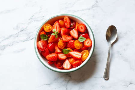Portion of strawberry and tomato cherry salad decorated with basil leavesの写真素材