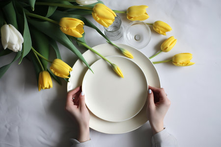 Woman's hands holding white empty plate, yellow tulips on the background, flatlay, mockup, Generative AIの素材