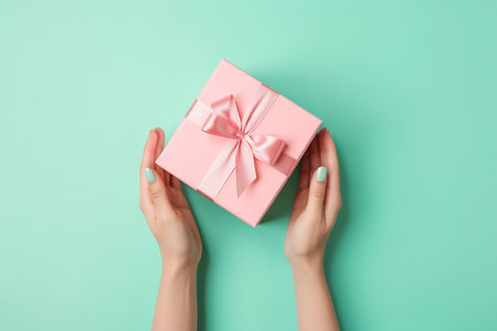 Female hands holding light pink giftbox on the green background, Generative AIの素材
