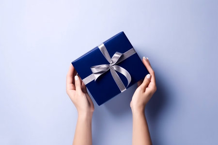 Woman hands holding blue giftbox with silver ribbon on the light blue background, top view, Generative AIの素材